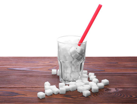 A complete glass of sugar cubes with long straw on a wooden table, isolated on a white background. Unhealthy sugar pieces on a brown table. The health risks related to diabetes and calorie intake.の写真素材