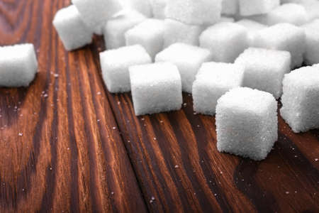 Sweet sugar cubes on a dark wooden table. A pile of white lumps of sugar cubes for cooking, baking, drinks and beverages. The health risks related to calorie intake.の写真素材