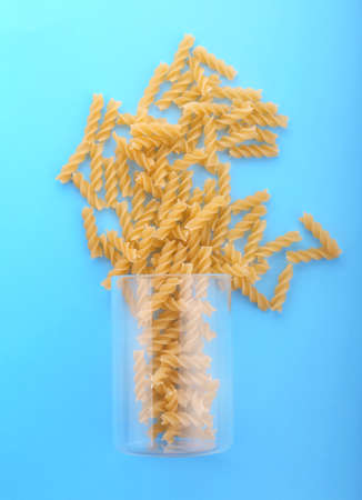 Uncooked Italian spaghetti pasta fusilli in big glass on the bright blue background. Hard and raw macaroni in the transparent glass. Organic yellow rigate pasta.の写真素材