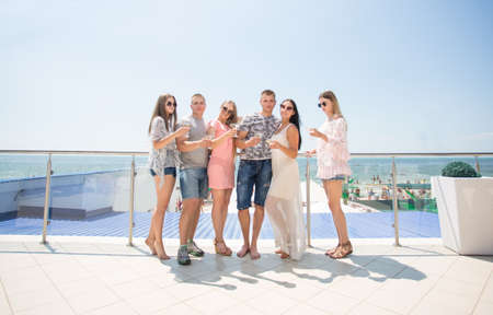 Happy friends in multicolored clothes having a party and drinking champagne at a luxury hotel near the beach. Summer beach party. Group of young people enjoying a summer beach party.の写真素材