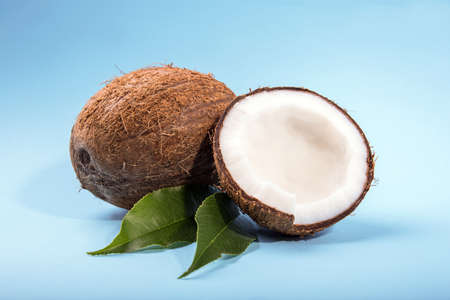 Coconuts with half and green leaves on a bright blue background. Ripe, fresh and appetizing coconuts. Organic fruits. Brown natural tropical and fresh fruit coconuts.の写真素材
