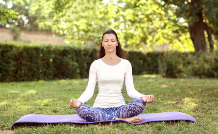 A calm woman in sportswear practicing yoga, sitting in Half Lotus exercise, Ardha Padmasana pose, working out, meditation session. Healthy lifestyle. Beautiful lady is sitting on meditation session.の写真素材