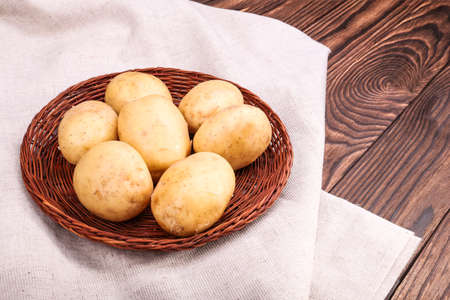 Raw and fresh vegetables. Close-up of organic new light brown potatoes on a light gray fabric and on a dark brown wooden background. Macro potatoes. Fresh agriculture food. Vegetable of potatoes.の写真素材