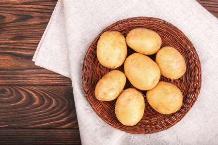 Fresh vegetables. Organic and uncooked new light brown potatoes on a gray fabric and a dark brown wooden table. Two big, tasty, fresh new potatoes on a gray fabric. Close-up of new brown potatoes.の写真素材