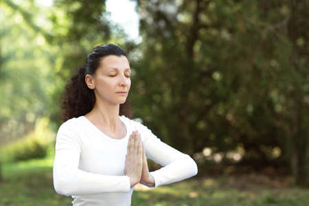 Close-up portrait of fitness woman is doing yoga with namaste. An attractive woman is practicing yoga. Female trainer in sportswear is doing asanas, working out, outdoor. Sporty and adult woman doing yoga practice.の写真素材
