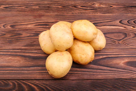 Uncooked, raw and fresh potatoes on a dark brown wooden background. Summer harvest of new potato tubers. Nutritious organic potatoes. Organic and uncooked new light brown potatoes. Fresh vegetables.の写真素材