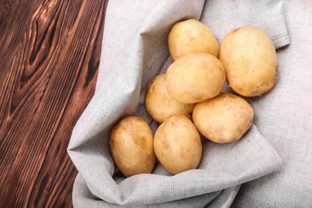 Organic and uncooked new light brown potatoes on a grey fabric and on a dark brown wooden background. A large pile of raw and young potatoes. Fresh vegetables. Summer harvest. Natural agriculture foodの写真素材