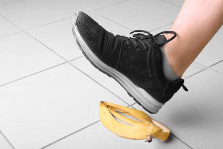 Male's leg in black trainers slips on a banana peel, on gray background. Bright yellow banana peel on the floor. Accident and risk concept.の写真素材