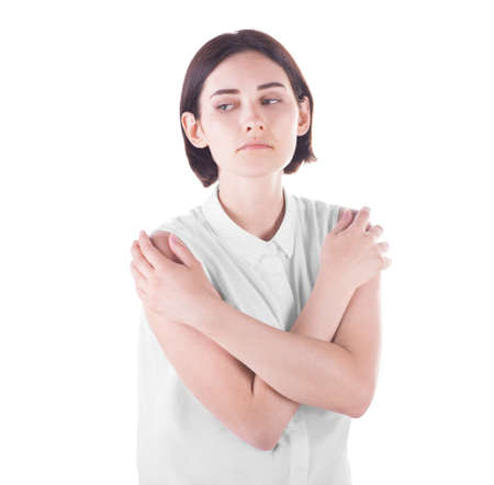 A cute and young girl in a white blouse holds her hands on her shoulders and looks thoughtful, isolated on a white background. A beautiful young woman in elegant blouse and with short dark brown hair.の写真素材