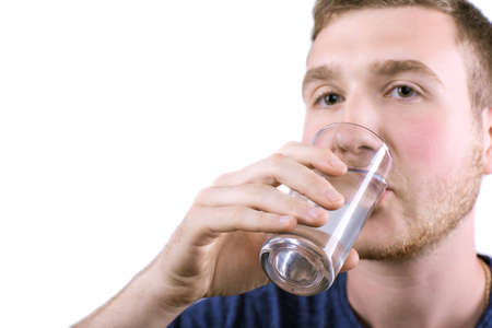 Clouse-up of a man taking prescripted medicine isolated over the white background. A young male drinking clear fresh water from a transparent glass. Medicaments to cure migraines, headaches.の写真素材