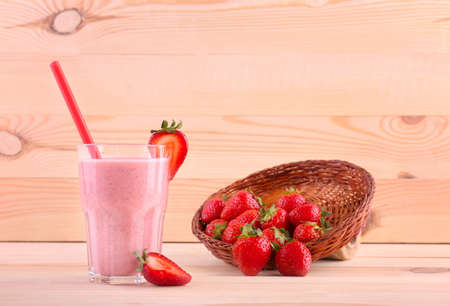 A summer beverage in a jar from sweet strawberries and fresh milk and a lot of bright red strawberries in a wooden basket. Bright pink cocktail and a basket full of strawberries on a light background.の写真素材