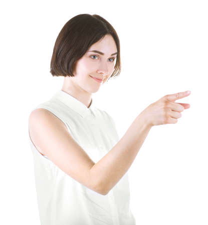 A positive brunette female isolated over the bright background. A cheerful girl in a light casual clothing pointing. A pretty young lady with short dark hair smiling.の写真素材