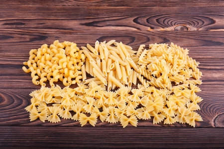 A variety of types of Italian pasta on a dark brown wooden table. Pasta is a staple food of...
