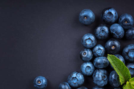 Top view of juicy and sweet blueberries with green leaves of mint on a dark background. Fresh, raw and ripe blueberries full of vitamins, close-up. Summer fruits from garden.の写真素材