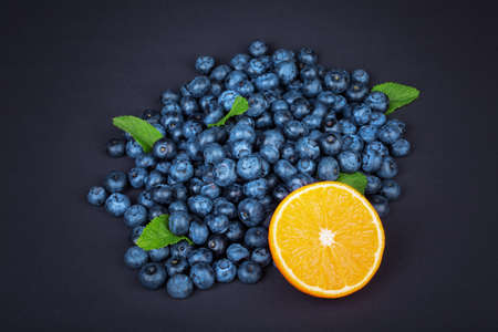 Summer half of orange with green leaves of mint near a heap of blueberries and on a dark background. Fresh and ripe blueberries and juicy half of orange with fresh mint.の写真素材