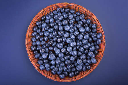 A view from above of sweet blueberries in a wicker wooden basket on a dark purple background. A lot of juicy and bitter blueberries in a brown crate. Tasty ingredients for cocktails. Summer fruits.の写真素材