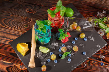 Top view picture of blue and red beverages on a wooden background. Refreshing bright cocktails with mint, lime segments, grapes, bilberries, strawberries, ice and carambola in transparent highball glasses.の写真素材
