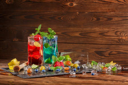 Refreshing blue and red beverages on a black table-napkin. Colourful cocktails with mint, slices of lime, berries, ice and carambola in transparent highball glasses on the wooden background.の写真素材