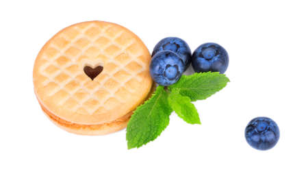 A view from above on a perfect light brown cookie with a heart. Juicy blueberries, mint leaves and crunchy biscuits isolated on a white background. Sugary and homemade organic snacks.の写真素材