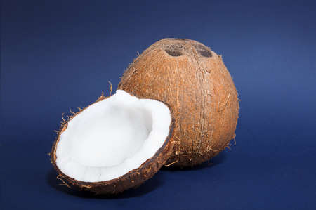 A pair of tasteful coconuts on a dark blue background. A close-up of a fresh coconut cut in half and...