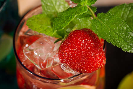 Top view of a refreshing tasty beverage with ripe strawberry slices, ice cubes and leaves of mint on a wooden background. Strawberry cocktail in a transparent glass. Delicious summer drink.の写真素材