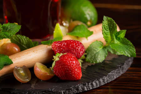 Close picture of colourful berries, lime, mint twigs and a pounder for cocktail ingredients on a black desk. Summer fruits on the wooden background. Tasty summer drinks with ripe fruits.の写真素材