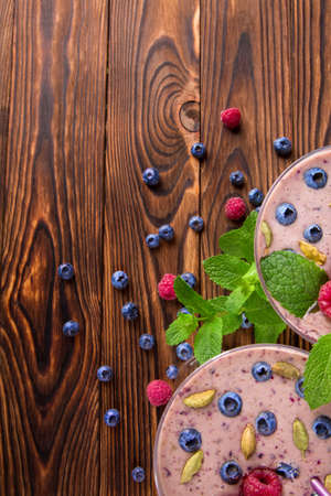 A view from above on pink smoothies with raspberries and blueberries on a wooden table background. A close-up of a blended fruit beverage with mint leaves and berries. Organic and healthy yogurt. の写真素材