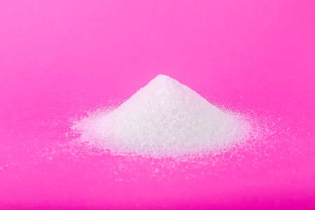 A pile of white organic sugar on a bright pink background. Sweet food ingredient for cooking, baking, and drinks. Unhealthy diet conception.の写真素材