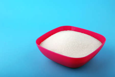 A bright pink box full of sweet rumbly sugar on a blue background. Consumption of bad calories. White organic sugar and sweet food ingredient. The sugar for cooking, baking and drinks.の写真素材