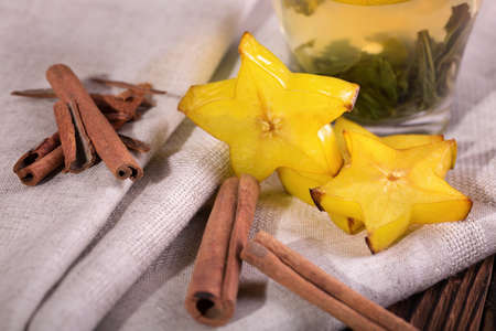 A close-up picture of healthy bright citrus carambola with fragrant cinnamon on a gray fabric table cloth. Perfect ingredients for healthy tea full of vitamins.  Exotic fruits.の写真素材