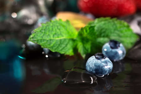 Close-up of bright dark blue blueberries on a black background. Raw and fresh blueberry with colorful mint and ice cubes. Natural summer ingredients for desserts and cocktails. Copy space.の写真素材