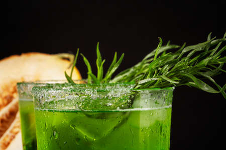 Close-up of delicious and refreshing alcohol beverages with lime pieces, spicy tarragon and ice...