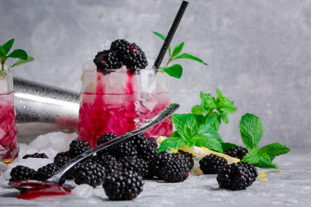 Close-up of a glass full of tasty, cold, beverage with blackberries, mint, lemon, and cubes of ice on a light gray background. The cocktail with black straw and berries. Copy space.の写真素材
