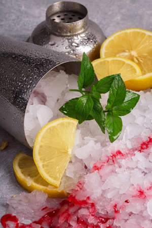 Close-up of ice shards on a gray blurred background. Crystal cubes in a metal cocktail shaker with bright mint leaves, jam and slices of lemon. Natural ingredients for summer beverages. Copy space.の写真素材