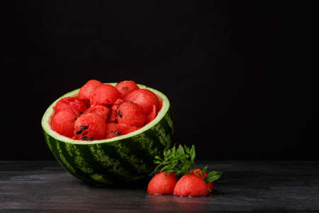 Colorful juicy watermelon on a table. Red watermelon scoops with green leaves on a black background. Summer juices. Copy space.の写真素材