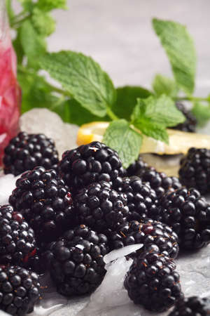 Close-up of ripe, cold, fresh, juicy blackberries on a frozen white table background. Crushed ice, purple blackberries, mint leaves and cut lemon. Rustic ingredients for homemade refreshing cocktails.の写真素材