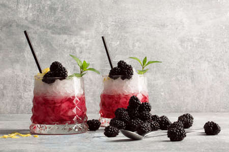 Two glasses of berry cocktails on a light gray background. Drinks with black straws, mint and blackberries. Copy space.の写真素材