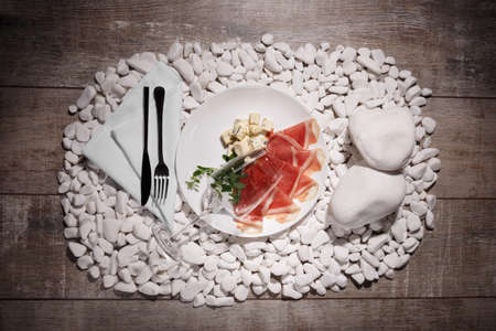 A white plate with hamon, blue cheese on white stones and on a wooden background. A transparent, empty glass near the food composition. Romantic dinner at the restaurant.の写真素材