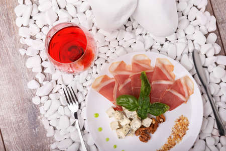 A plate with prosciutto, basil, and blue cheese on a white stone background. A glass of semi-sweet bright red wine near the expensive dish. Business dinner at the restaurant.の写真素材