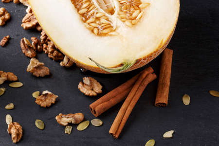 A top view composition of a fresh raw melon with cinnamon sticks, seeds and walnuts on a black...