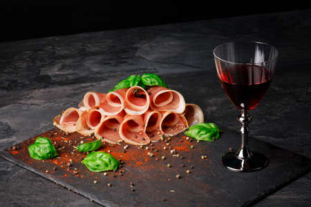 A close-up of a red wine glass and cut ham with spinach and pepper on a black background. Healthy, delicious and sweet wine.の写真素材