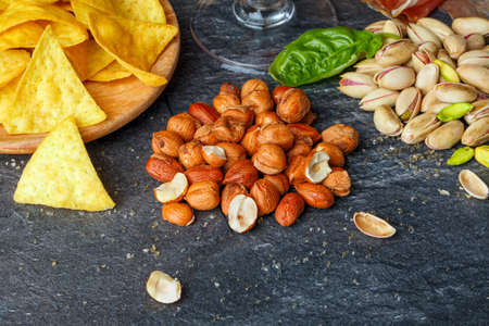 Close-up picture of delicious nachos, roasted peanuts, and bright pistachios on a dark gray background. Savory snacks for beer.の写真素材
