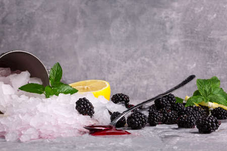 Beautiful shiny white ice cubes. Ice with ripe blackberries, sour lemon, dessert spoon, and berry...