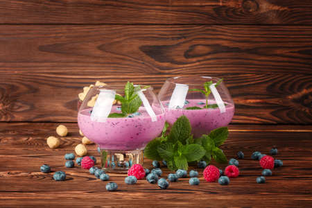 A couple of spacious glasses with tasty, refreshing, blended fruit cocktails on a brown wooden background. Sweet blueberries, raspberries and crunchy peanuts next to dairy sweet yogurts. Copy space.の写真素材