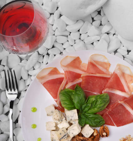 Close-up of a glass of dry red wine and a plate with salted and raw prosciutto or balyk, basil, and blue cheese on a white stone background. Top view of expensive snake.の写真素材