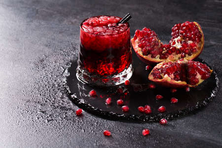 Organic pomegranate broken down into parts on a dark gray background. The transparent glass filled with fresh, sweet and useful garnet juice, ice and with black straws. Beneficially vitamins.の写真素材