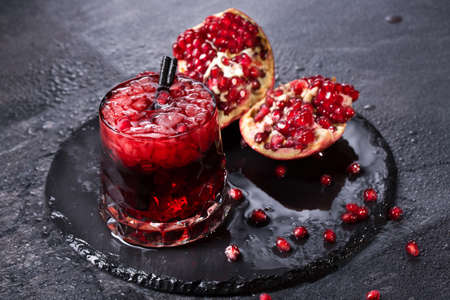 Organic pomegranate broken down into parts on a dark gray background. The transparent glass filled with fresh, sweet and useful garnet juice, ice and with black straws. Beneficially vitamins.の写真素材
