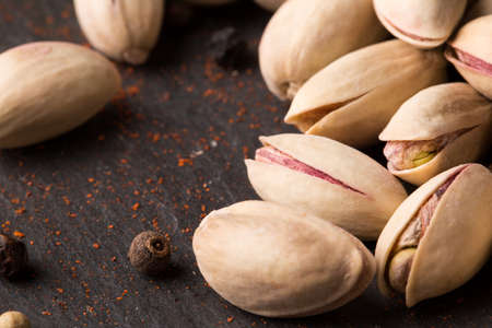 Close-up of a heap of crunchy pistachios and spicy pepper on a black table background. Traditional restaurant ingredients. Salted pistachio nuts for a party or celebration.の写真素材