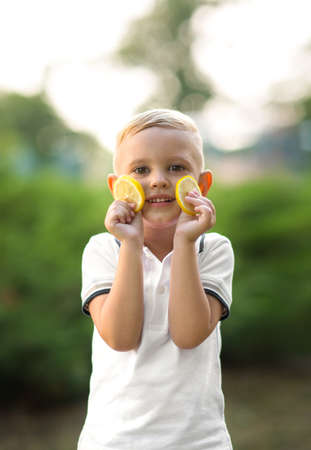 A cute little kid. Healthy and happy family. A young boy holding lemons on a green park background. Making lemonade.の写真素材