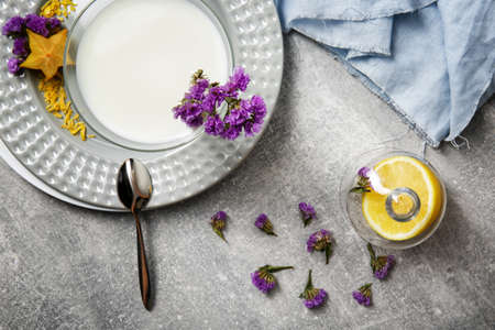 A view from above of a composition of summer dessert. A glass of white, organic milk smoothie or yogurt with blue fabric, purple flowers and exotic carambola on a light gray background.の写真素材